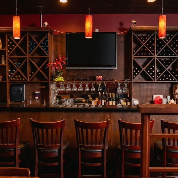 A sushi restaurant bar with wine racks, a TV, hanging glasses, and bar stools.