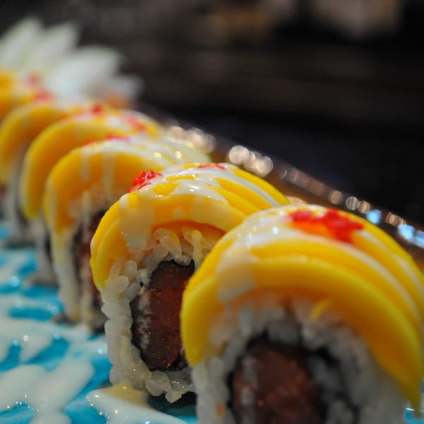 Close-up of mango sushi rolls with white sauce and red roe on a blue patterned plate.