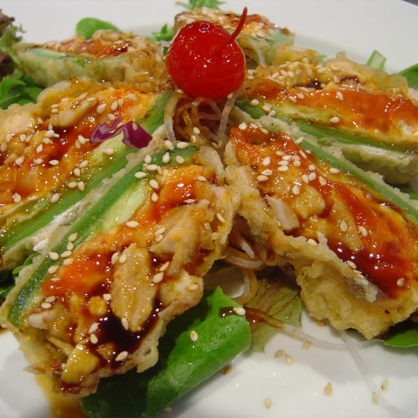 Tempura-fried avocado slices with sweet sauce, sesame seeds, and a maraschino cherry garnish.