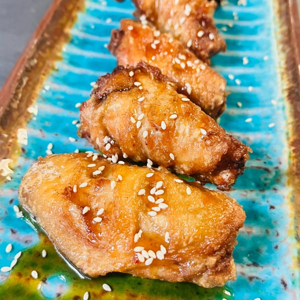Four crispy chicken wings with sesame seeds and green sauce on a blue and brown plate.